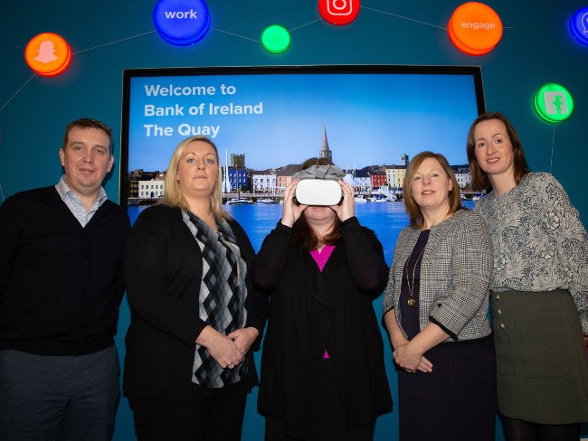 A man and four women, one of them wearing a VR headset.