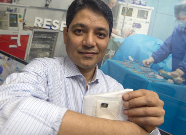 Man in shirt holds a biosensor patch over his arm.