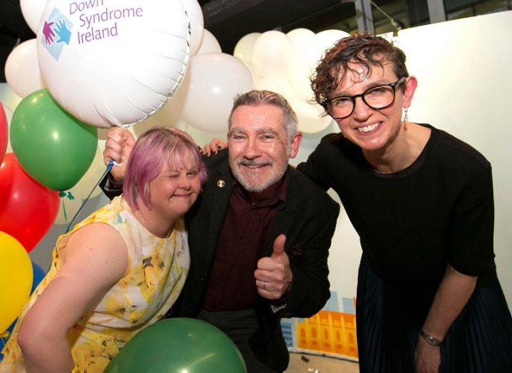 Two women and a man surrounded by balloons celebrating.