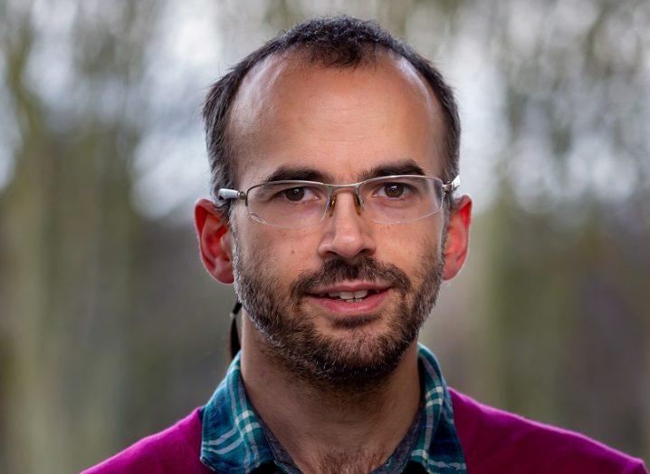 Konstantinos Gkrintzalis wearing glasses and a purple jumper against a blurry tree background.