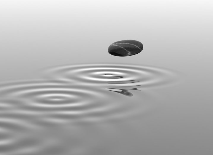 Greyscale image of a rock skipping across water leaving a trail behind it.