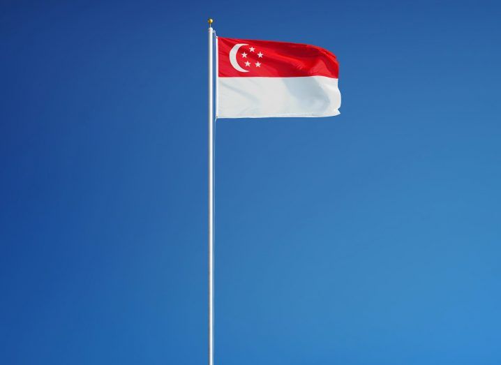 View of a Singapore flag billowing in the breeze on a silver flagpole against a cloudless blue sky on a bright day.