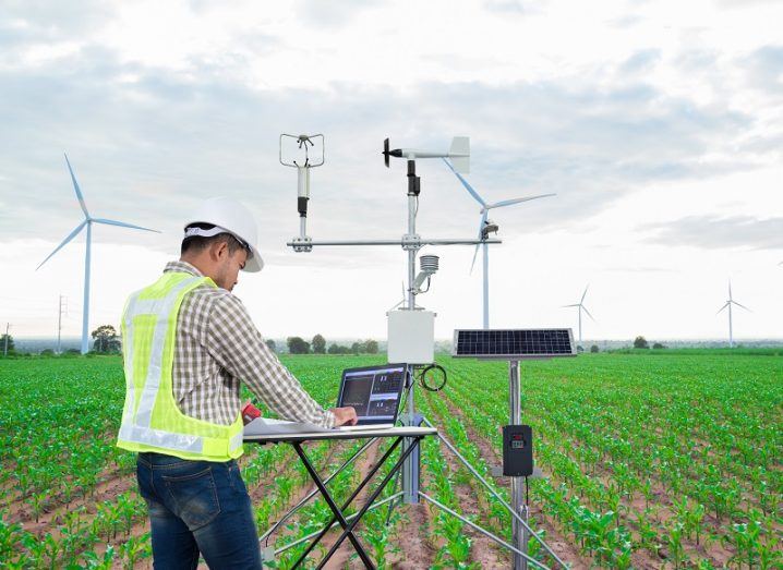 Researcher in high-vis jacket analysing lab equipment in a field with windmills in the background.