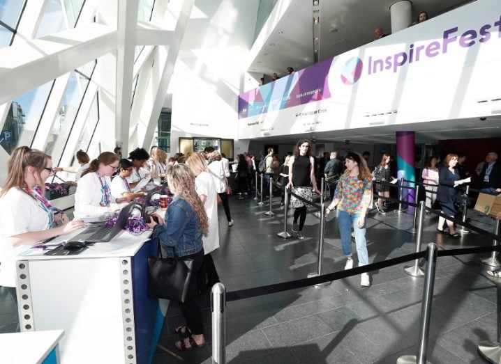 People queuing at Inspirefest 2018 in brightly-lit glass theatre.