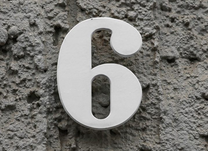 Close-up of a white number six against a grey concrete wall.