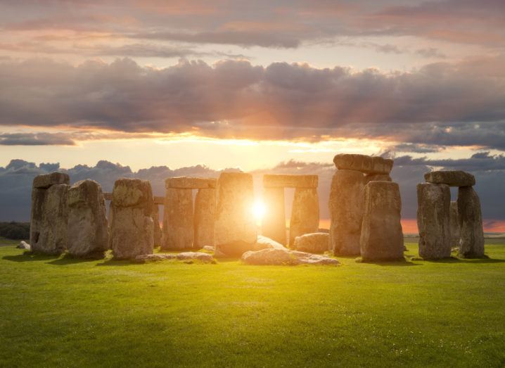 The sunrise streams from behind the large rock structures of Stonehenge during the summer solstice.