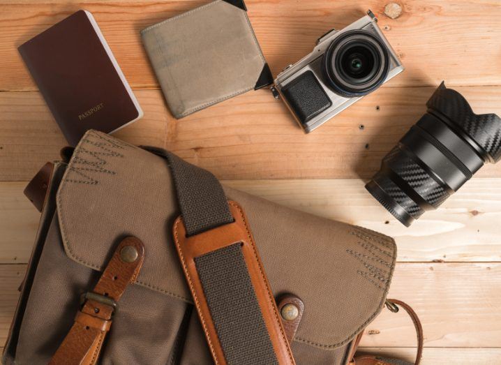 Overhead view of a camera, wallet, duffel bad and other travel paraphernalia on a wooden table.