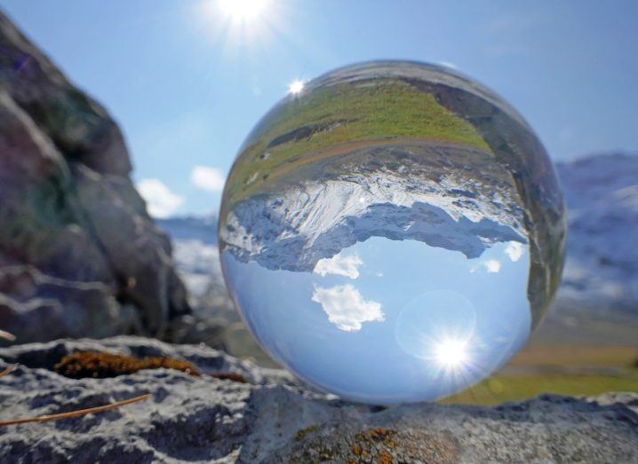 A crystal ball placed on a rock reflecting a mountain range and sunny sky.