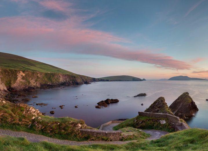 Scenic, panoramic shot of rocks and a steep road descending to a quay against a dusk sky.