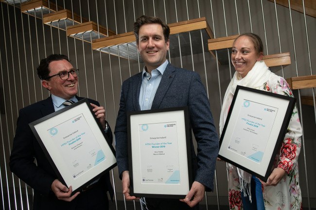 Two men and one woman smile proudly as they hold up certificates they were awarded from Enterprise Ireland.