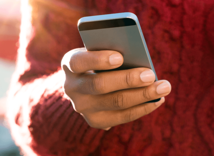 A person in a red sweater holds an iPhone.