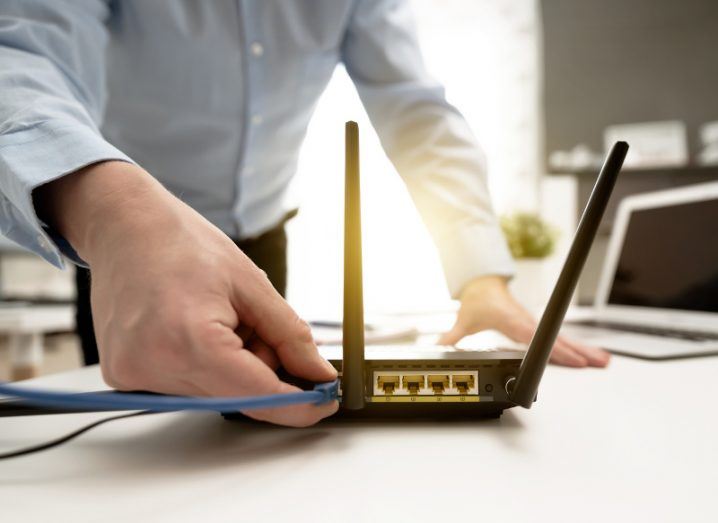 Man in business shirt plugging a wire into his broadband modem because he finally has fibre broadband.