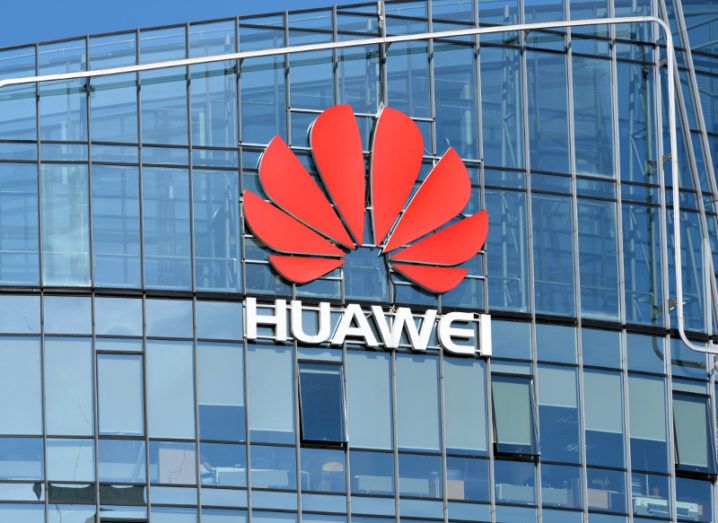 View of red lotus Huawei logo with company name in white capitlaised text underneath on glass building front.