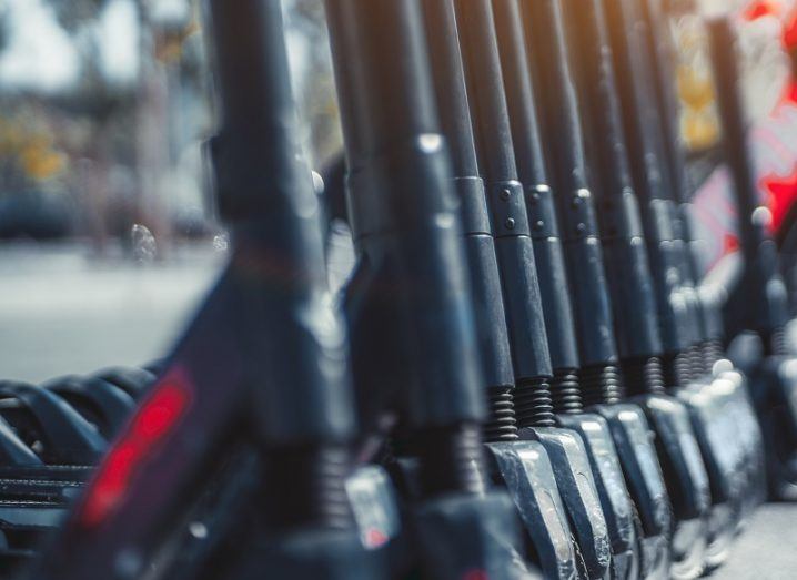 Row of black and red e-scooters lined up on the side of a footpath.