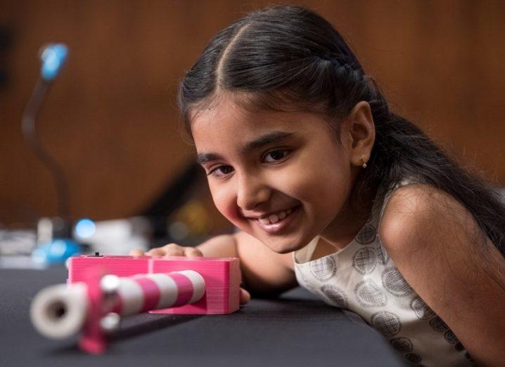 Mihika Sharma smiling while looking along the length of her pink and white Smart Stick on a table.