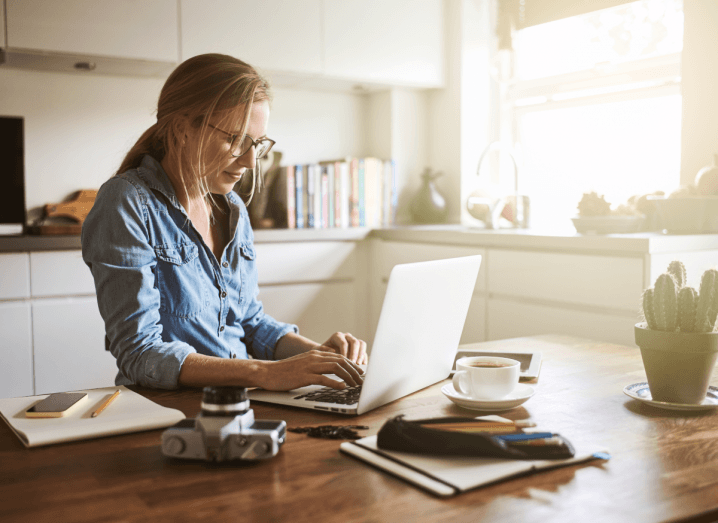 A woman works from home. She is on a laptop in her kitchen.