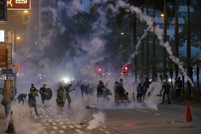 Protest scene with protesters throwing back tear gas at police. 