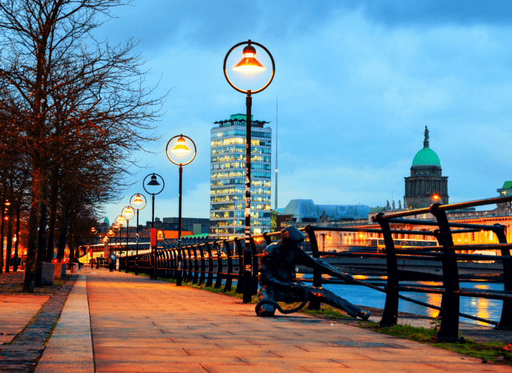 Dublin's quays at dusk in autumn, trees have no leaves and the streetlights are lit along the Liffey leading up to the Sean O'Casey Bridge and Liberty Hall.