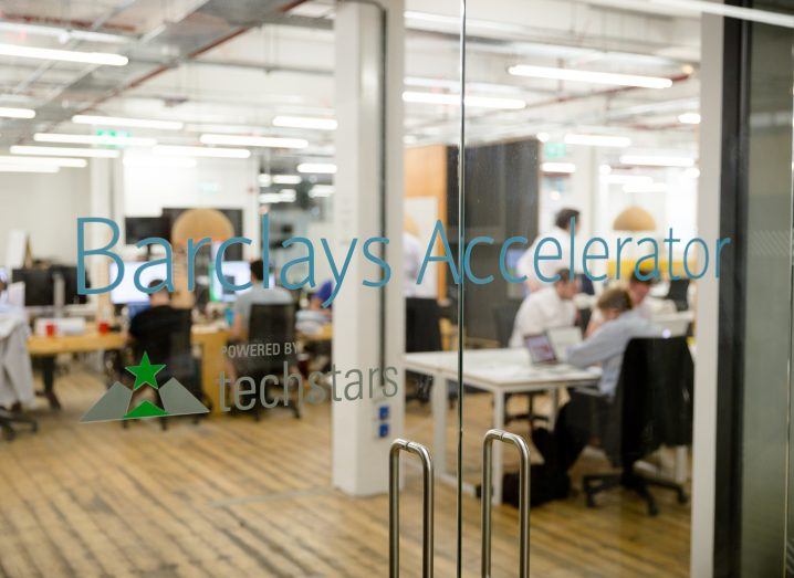 A clear glass door looking into an office space where workers are sitting at their desks. On the door it says Barclays Accelerator.