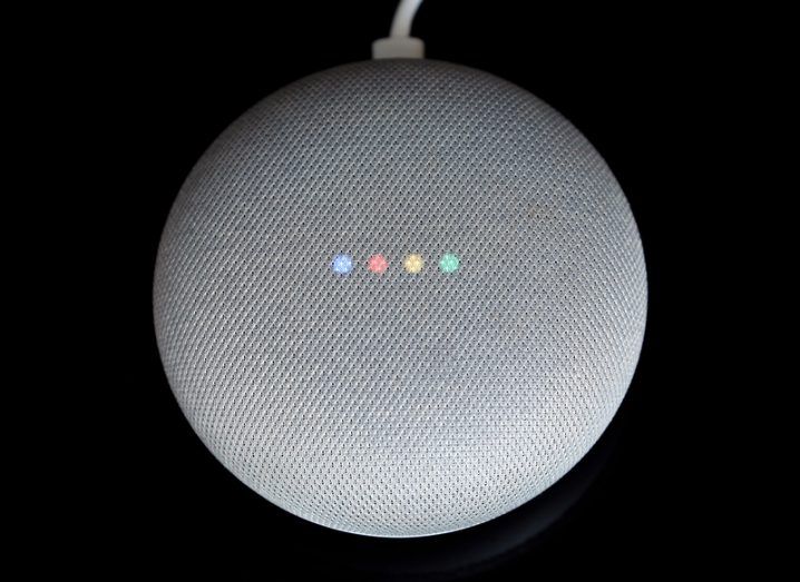 Overhead view of a small round speaker with four faint lights in blue, red, yellow and green on its surface.