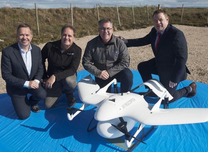 Four men smiling beside the medical delivery drone on a blue tarp.