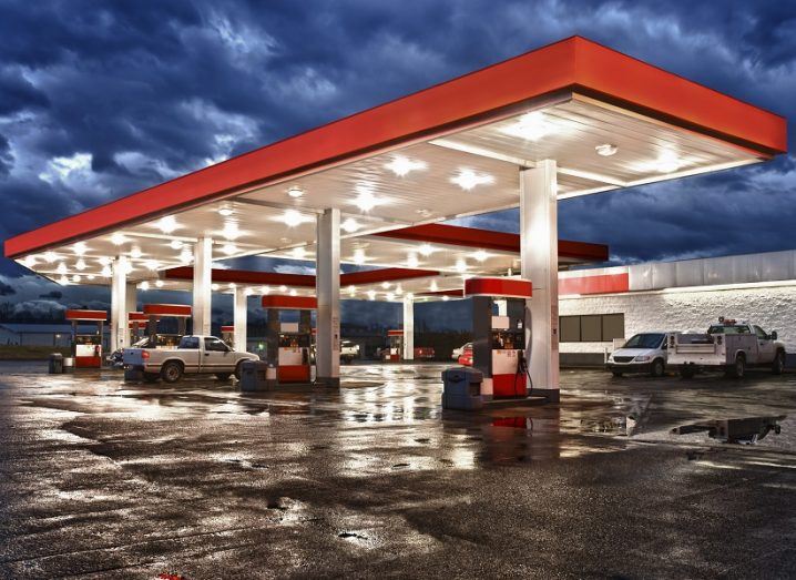 A red and white petrol station lit up by lights on a dark, cloudy night.