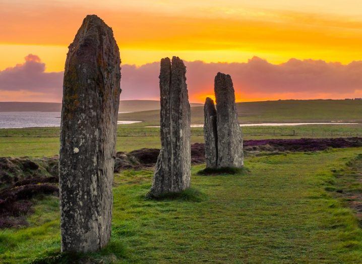 Three ancient standing stones on the Shetland Islands against a yellow dusk sky.