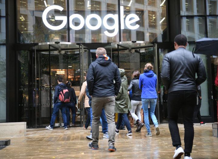 View of people walking into building with glass facade and Google logo above the door on a wet day.