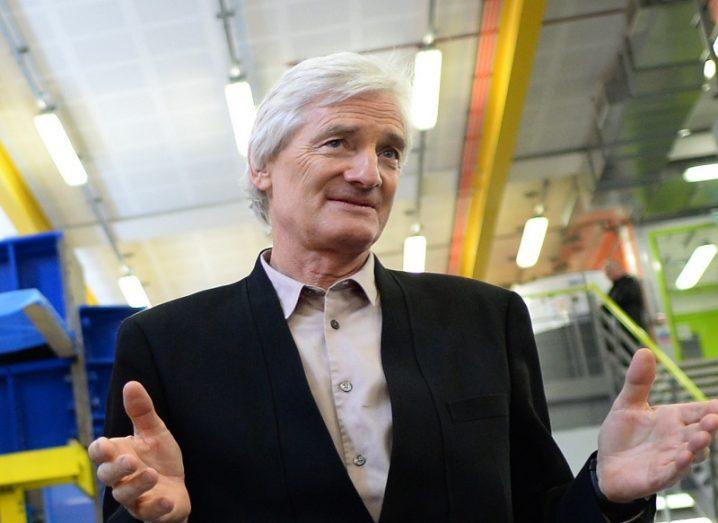 James Dyson wearing a black blazer and white shirt holding his hands out.