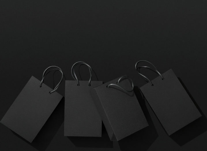 View of black shopping bags lying flat against darker black background.