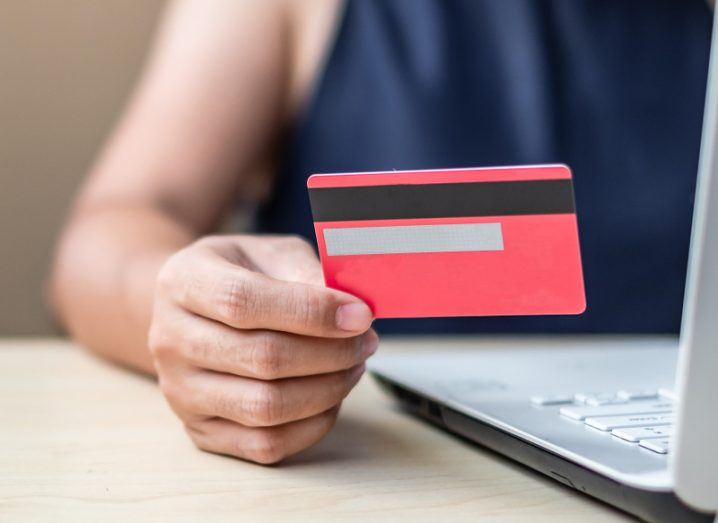 A woman’s hand holding a credit card as she inputs the data on a laptop to complete an online transaction.