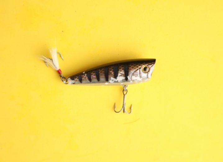 A mock fish fishing lure with three-pronged hooks dangling from its belly and its tail.