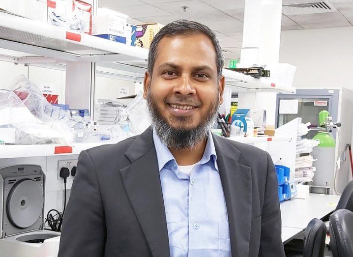 Dr Kabir H Biswas smiling in a grey blazer and blue shirt in his lab.