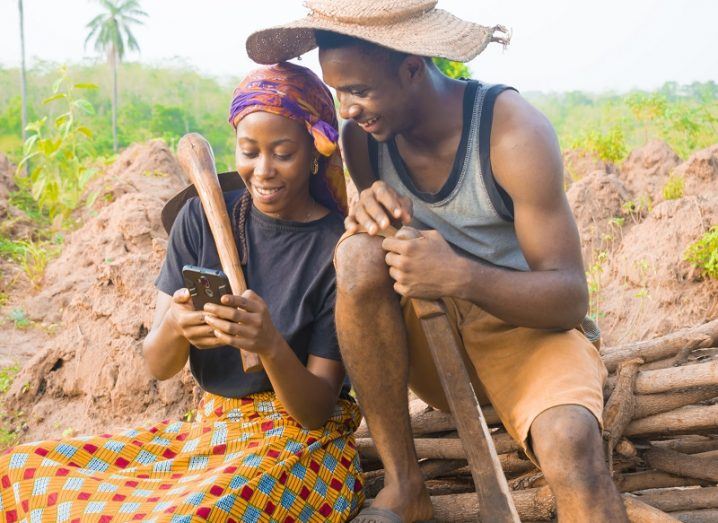 Rural African couple smiling while looking at a mobile phone.