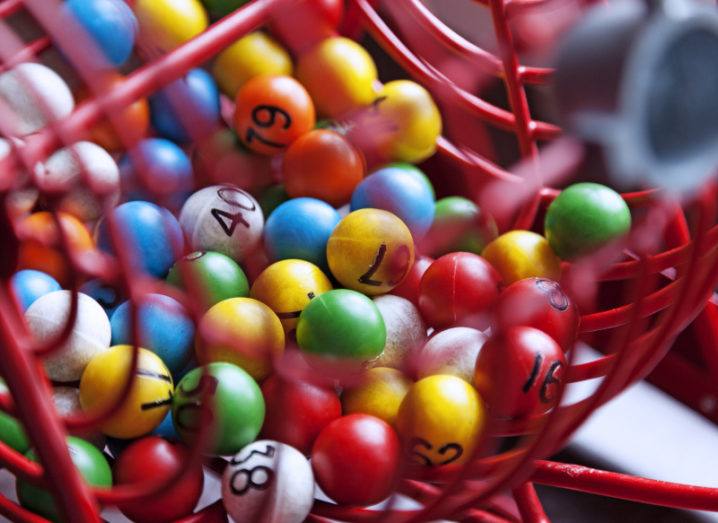 Close-up of a red-wire lottery drum filled with colourful numbered balls.