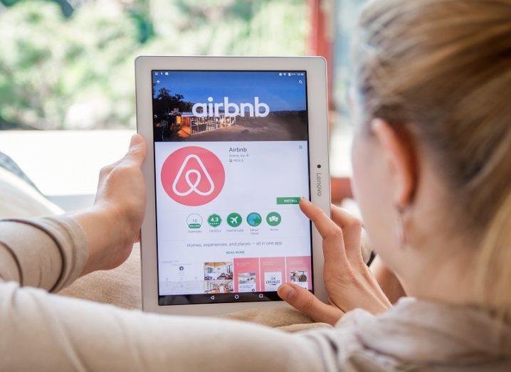 Person sitting on a couch looking at the Airbnb app on a tablet.