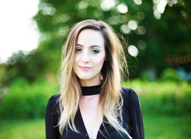 Caitlin Vander Weele in a black top wit black neckband, smiling, against a grassy background. 