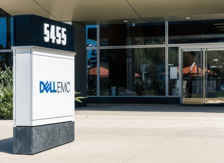 The exterior of a Dell office building in Santa Clara. It has a glass front door and there is a large pillar with the Dell logo outside and some potted plants.