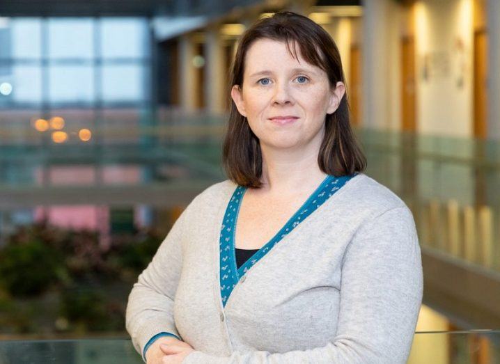 Emma Whelan in a grey cardigan and turquoise shirt smiling against an open-plan campus hall.