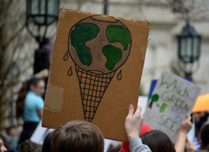 Close-up of a cardboard sign raised above a crowd at a climate protest, depicting Earth as a melting ice cream cone.