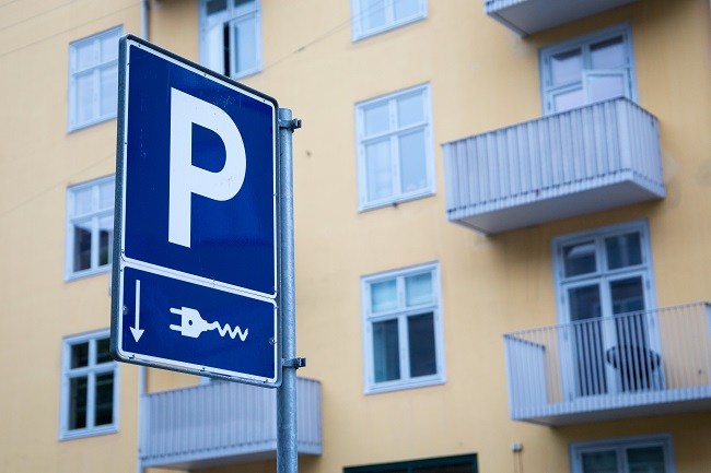 A blue parking sign with a charging point indicator beneath with an apartment block in the background.