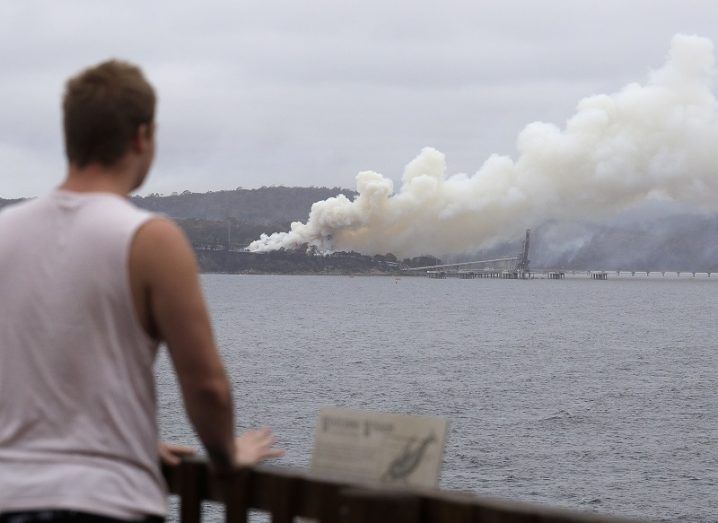 View of a man looking across a body of water at a plume of smoke from the Australian wildfires.