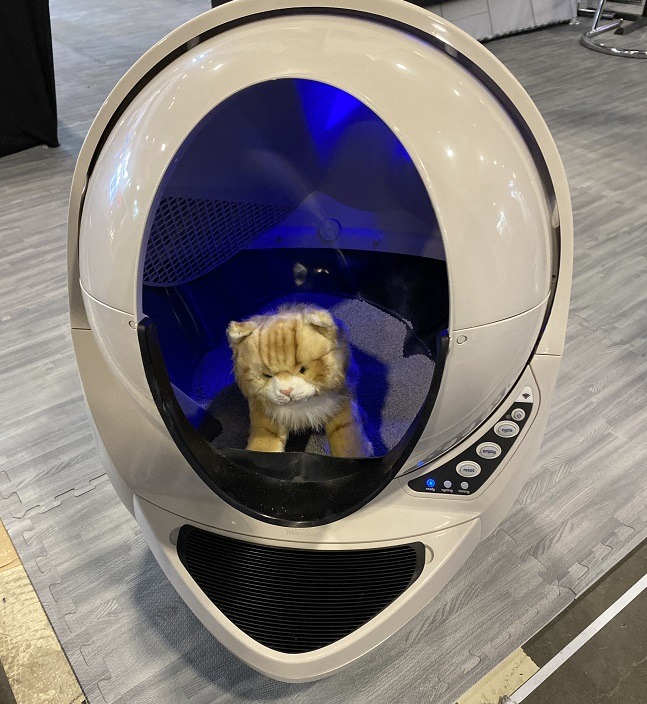 A toy cat sitting in the orb-shaped litter tray device. 