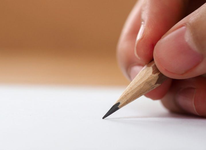 Close-up of fingers gripping a pencil with the tip touching a page.