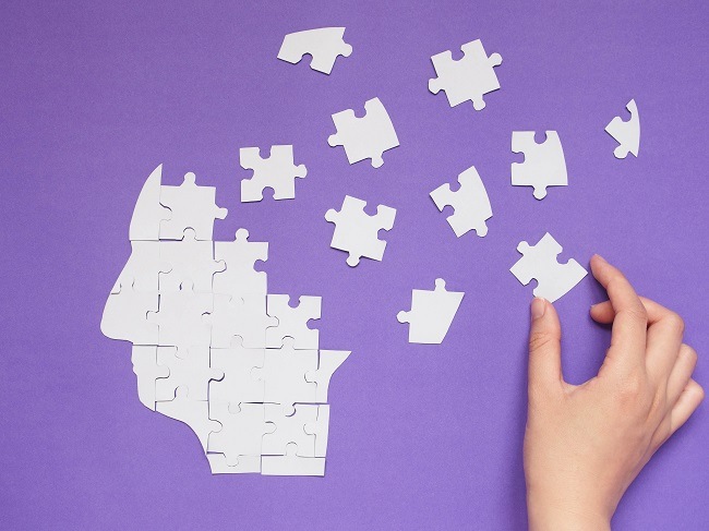 A hand putting together a head-shaped jigsaw puzzle against a purple background.