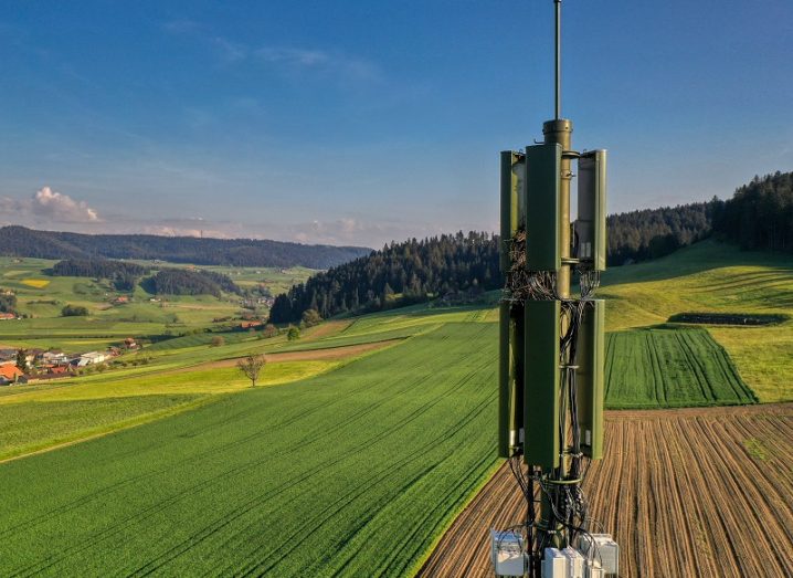Green 5G mast in the foreground with rolling, Swiss fields in the background and a blue sky.