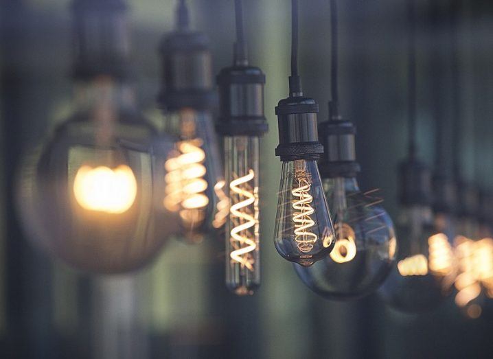 A row of lightbulbs, each a different shape and size, are lit and hanging from a ceiling.