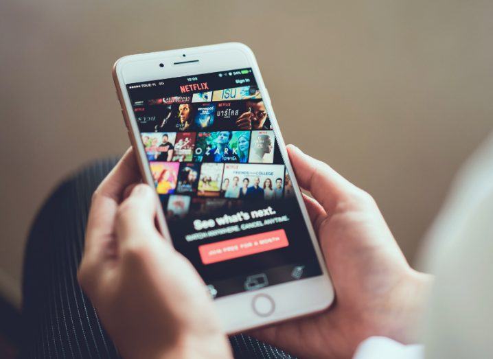 A woman’s hands holding a smartphone with the Netflix app open.