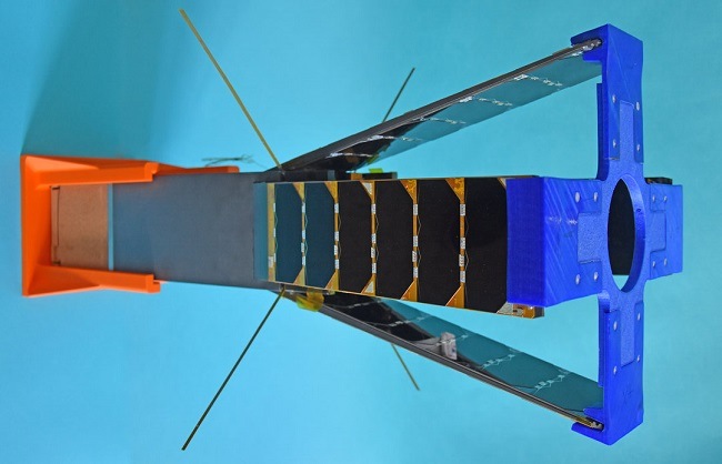 A long cubesat with fins to increase drag during re-orbit and a square orange top on one end and a blue cross on the other. 