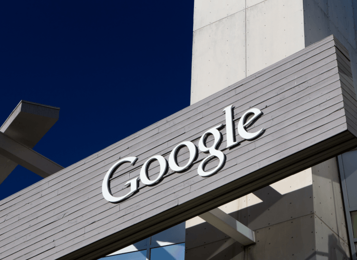 The Google logo on the facade of a grey building under a blue sky.